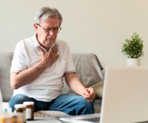 Older man sat on the sofa experiencing acid reflux and holding his chest