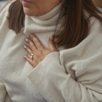 Mature hispanic woman with discomfort at home, hand on chest, in a cozy living room.
