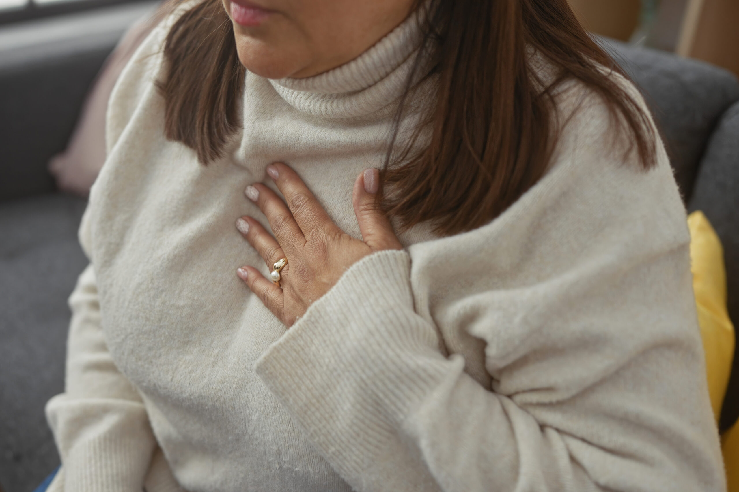Mature hispanic woman with discomfort at home, hand on chest, in a cozy living room.